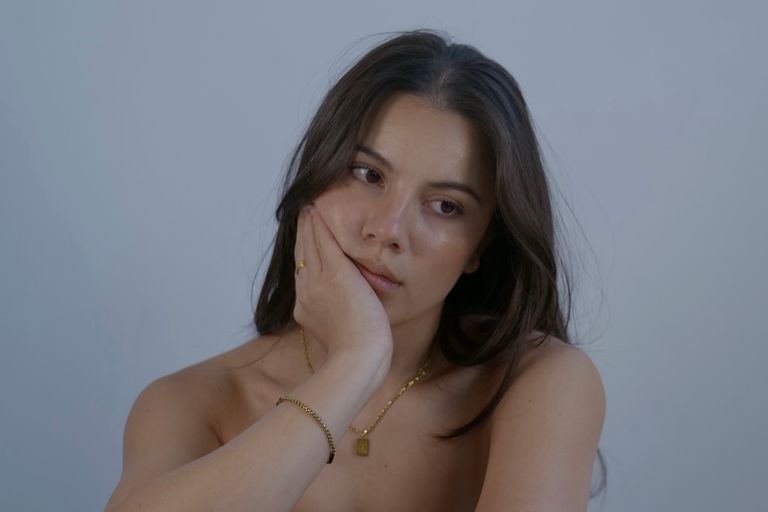 Promotional portrait of musical artist Meila resting her head on her hand against a simple gray background.